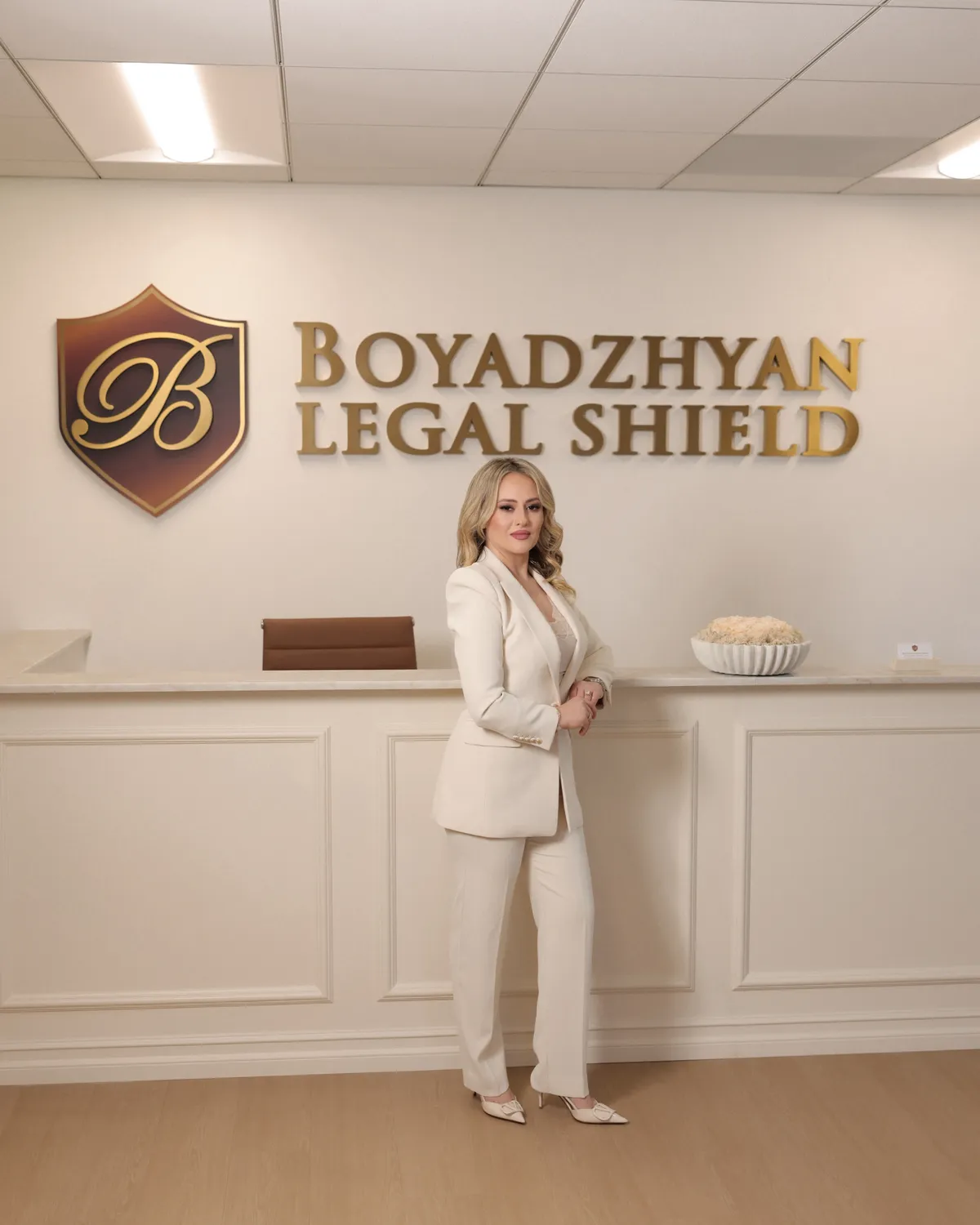 Knarik Boyadzhyan standing in front of the Boyadzhyan Legal Shield reception wall